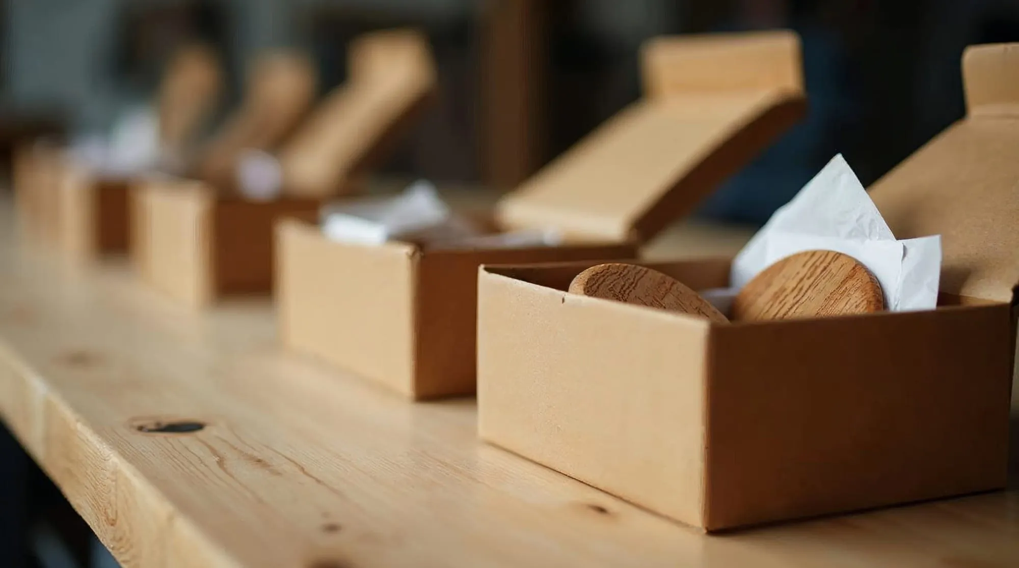 Coffrets kraft alignés sur une table d'atelier, l'un ouvert sur des dessous de verre